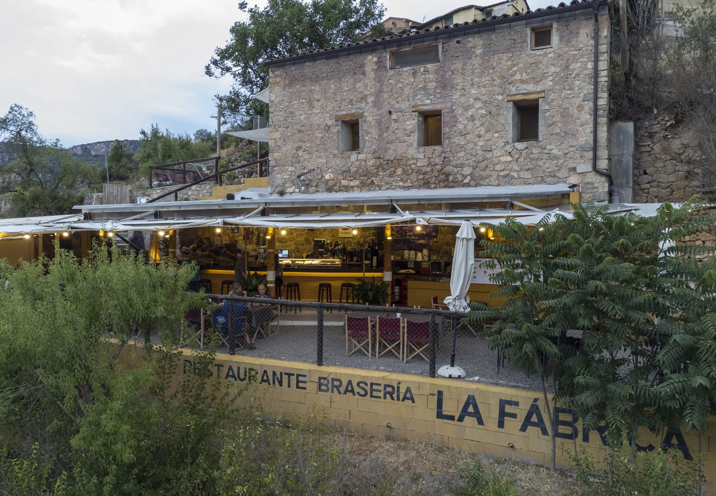 Vista aérea del restaurante iluminado al anochecer, con el cartel de La Fábrica