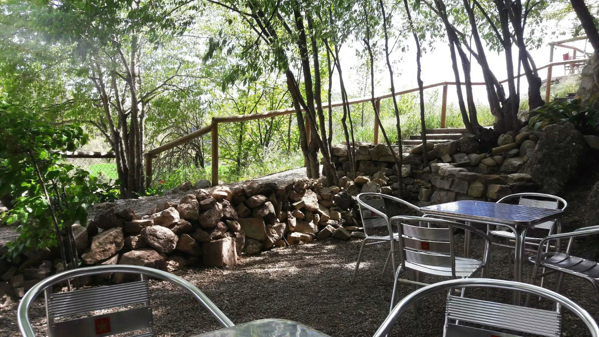 La Arboleda — mesas a la sombra entre piedra y árboles