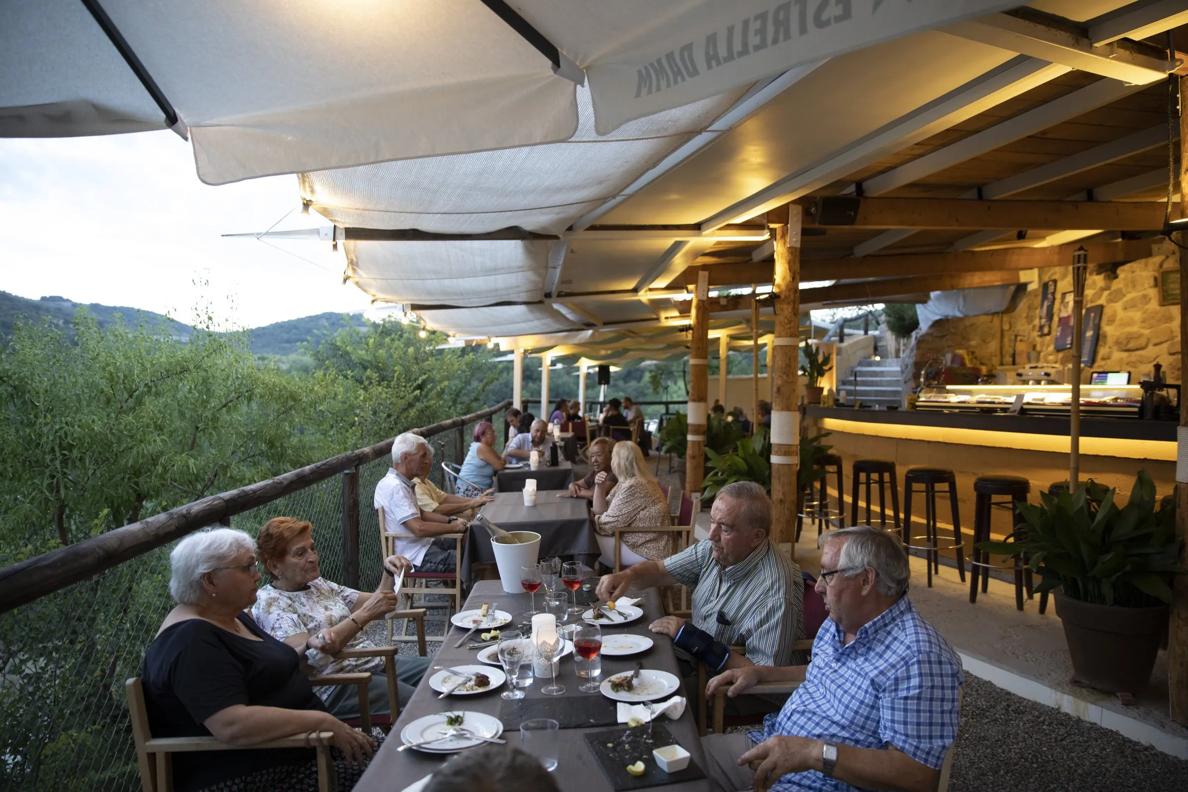 Terraza llena de comensales al atardecer, bajo los toldos y las guirnaldas de luz